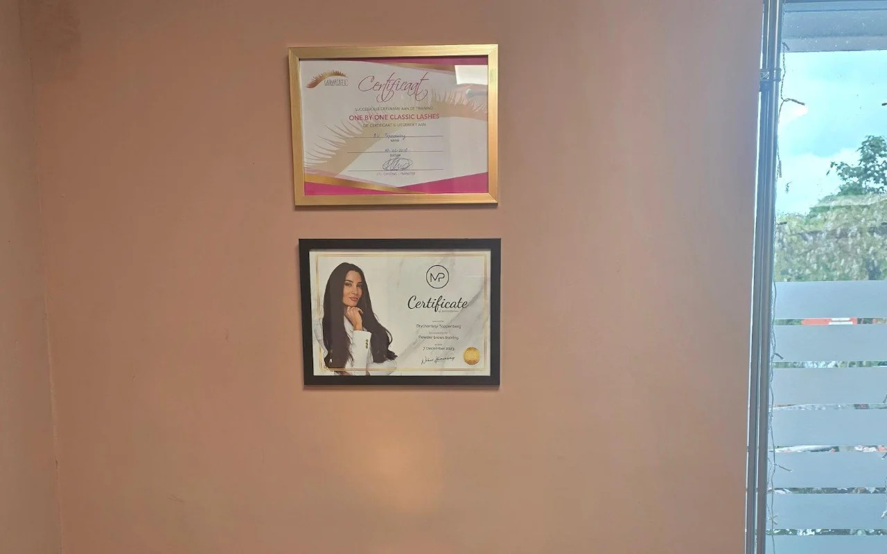 Twee ingelijste certificaten aan de roze muur van de salon